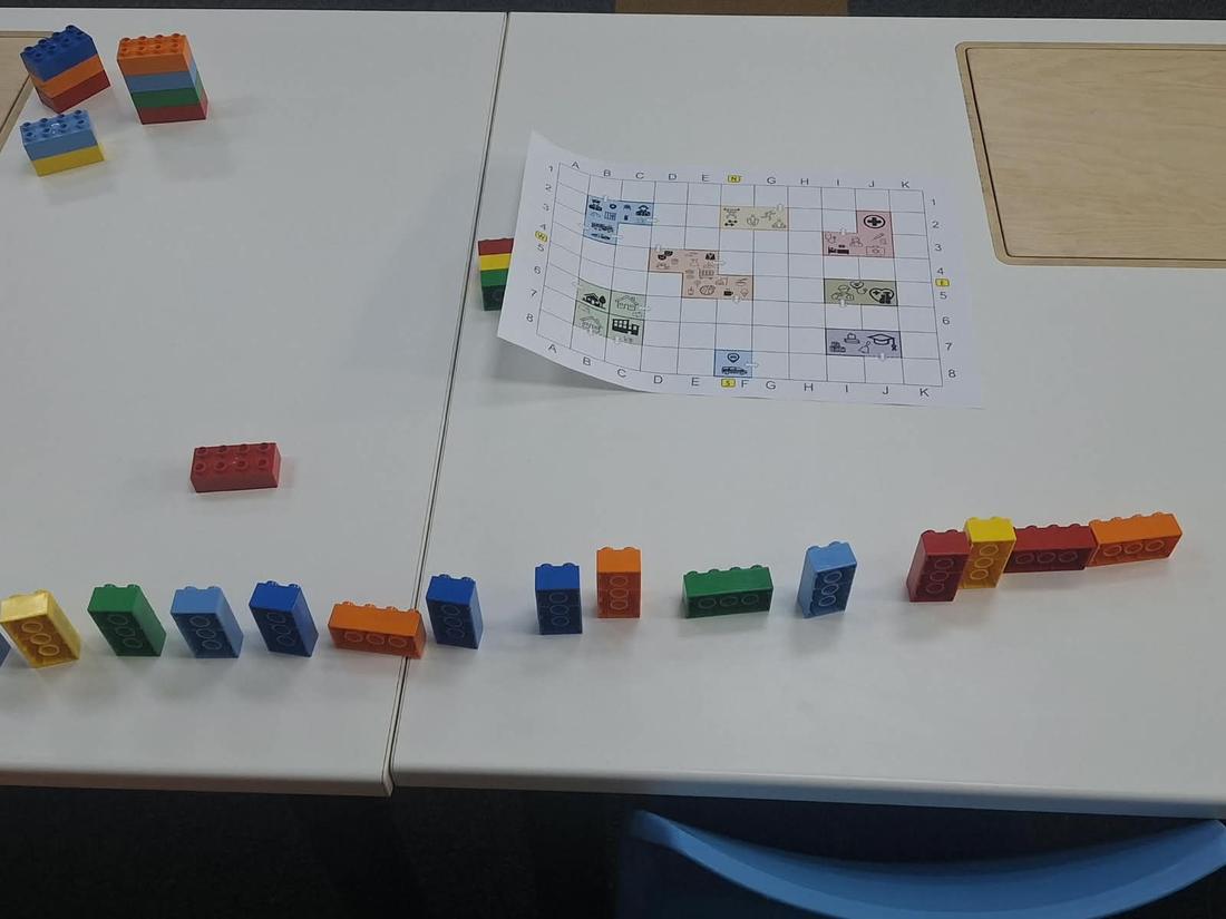 A paper coordinate grid on a table with a start brick and a long row of instruction bricks laid out as a program