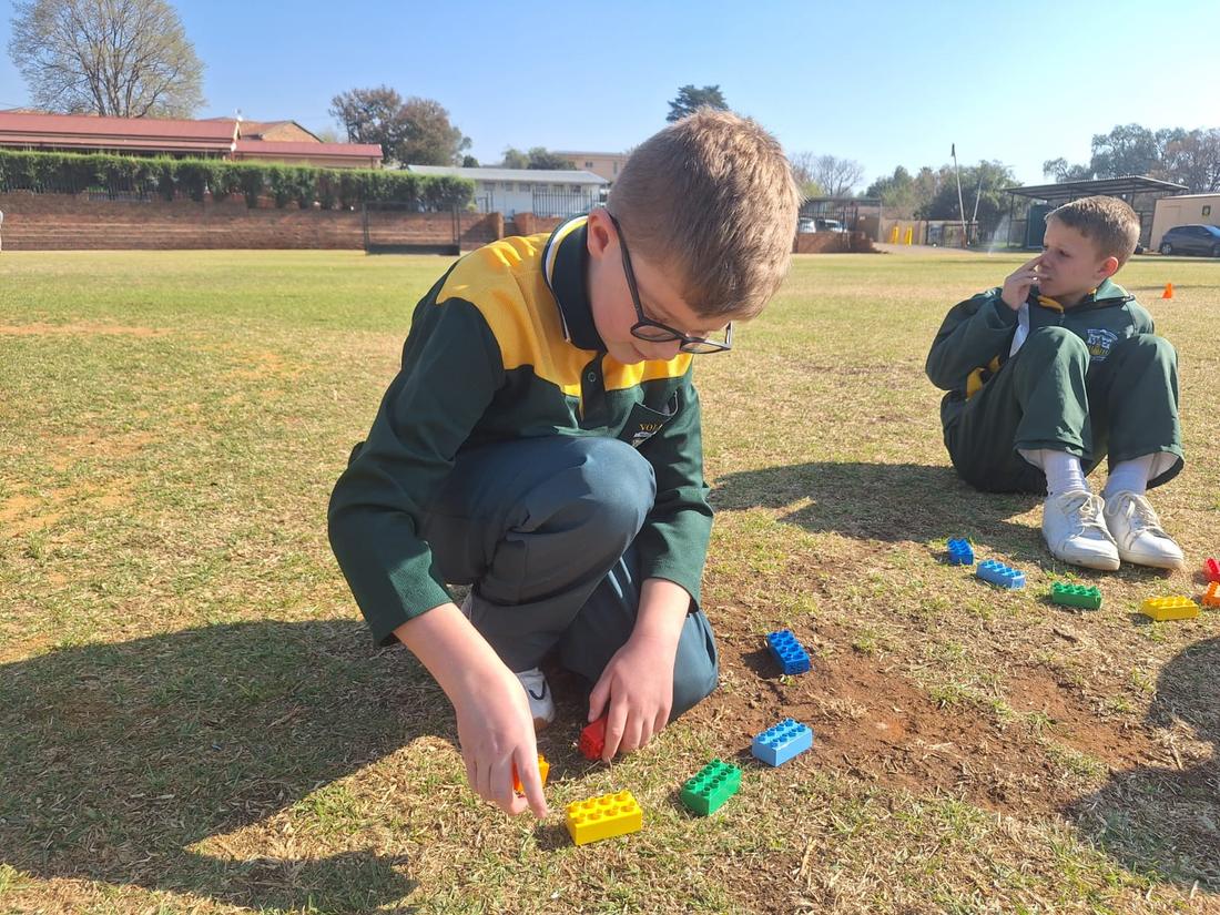 A pupil kneels on a school field arranging a line of coloured bricks as a program
