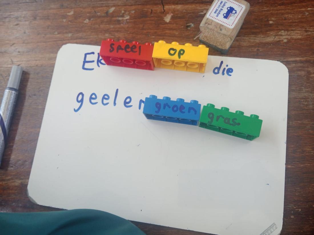 Coloured word bricks spelling an Afrikaans sentence, Ek speel op die geel en groen gras