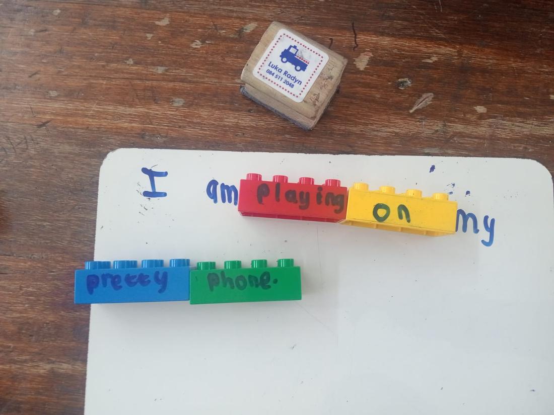 Coloured word bricks on a small whiteboard spelling the sentence I am playing on my pretty phone