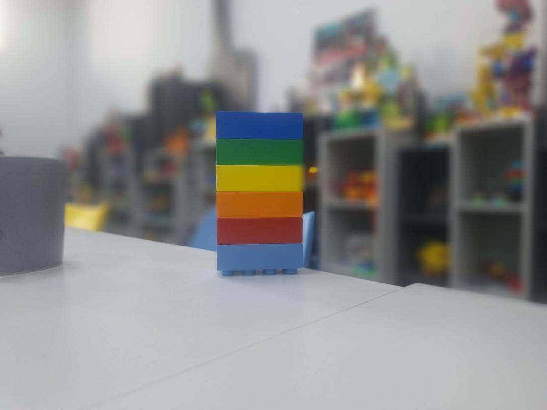 A stack of six coloured DUPLO bricks on a table, a play room of models blurred behind